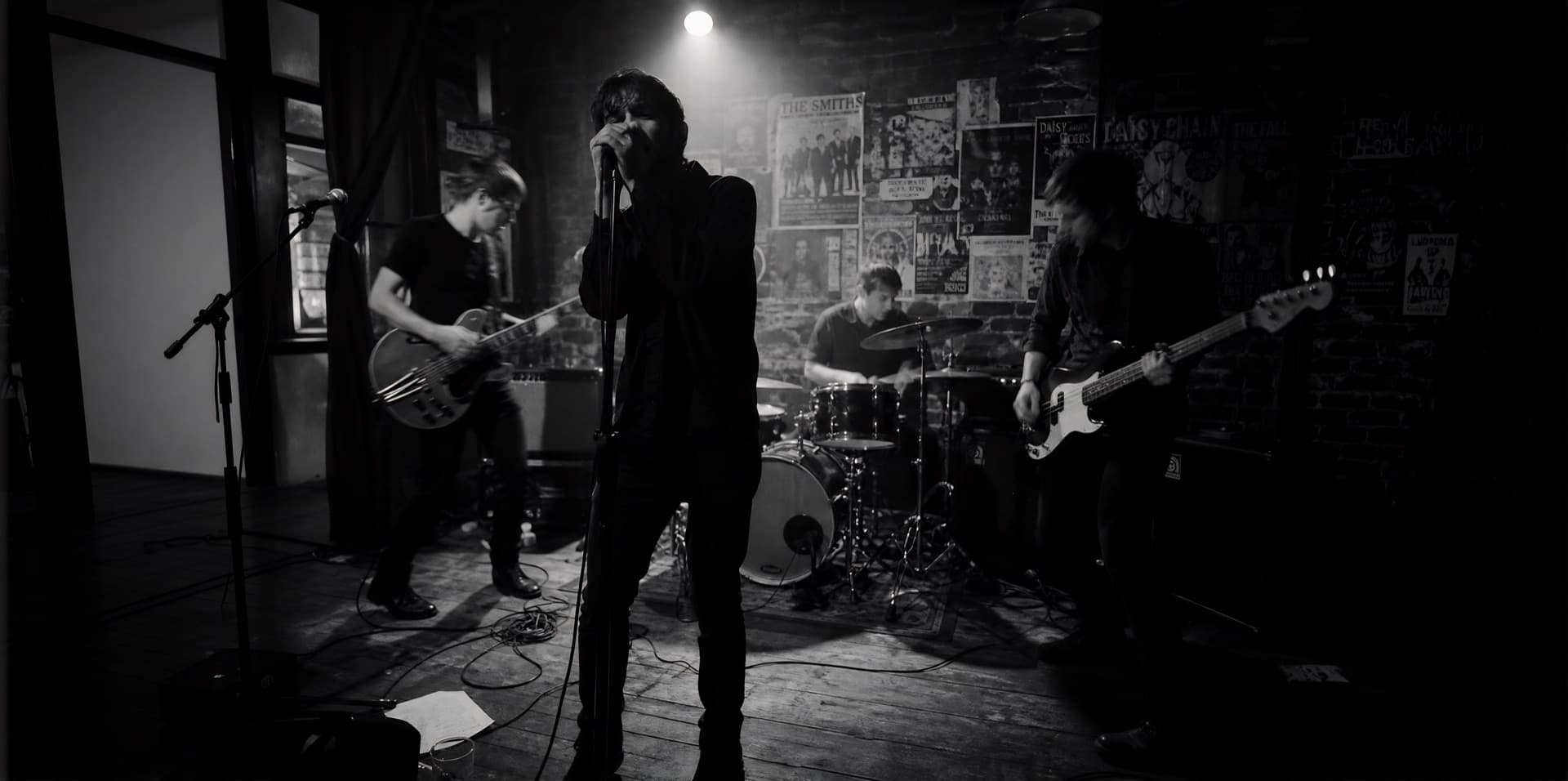 A garage-rock band playing a small brick-walled club in black and white, singer at the mic